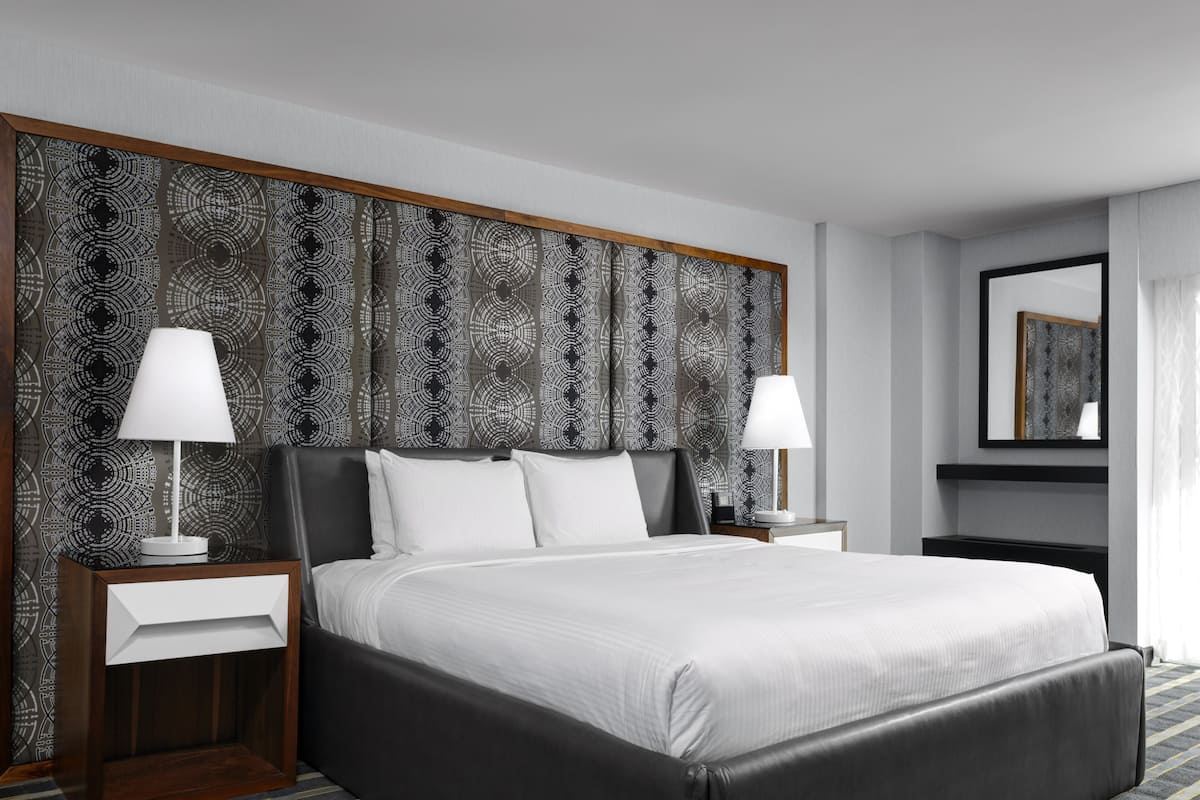 A modern hotel room with a large bed, two bedside tables, and a patterned headboard.