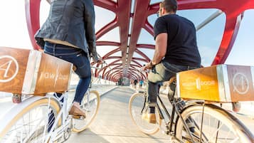 Two people riding bicycles with delivery boxes labeled "rawbar" and "yellow door" on a bridge with a red metal structure.