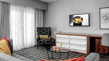 Una sala moderna con sofá, sillón, mesa de centro y comedor con un tazón de fruta y un vaso de jugo.