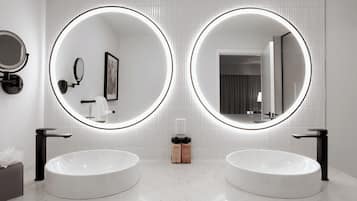 A modern bathroom with two round mirrors, a white sink, and a towel dispenser.