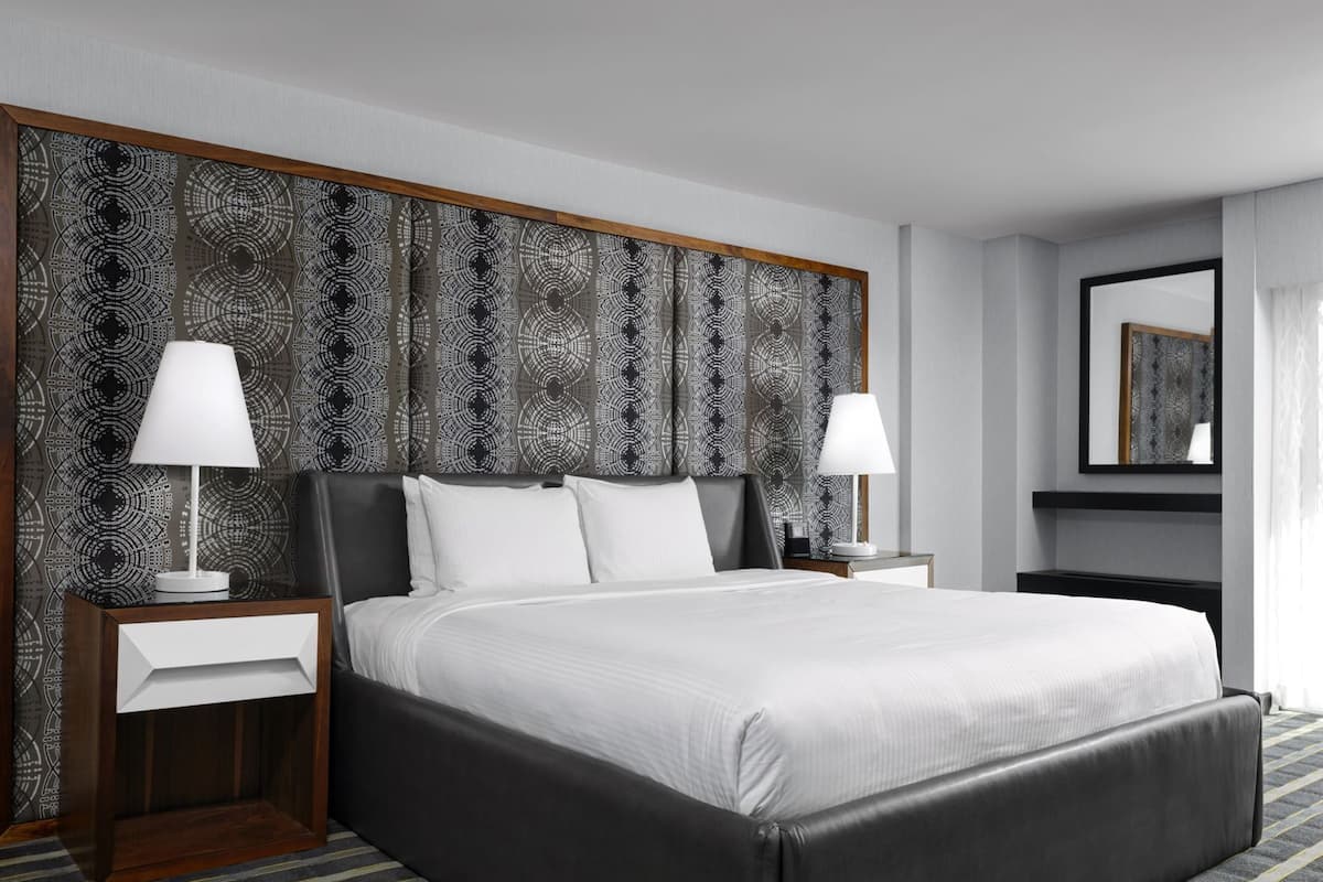 A modern hotel room with a large bed, two bedside tables, and a patterned headboard.