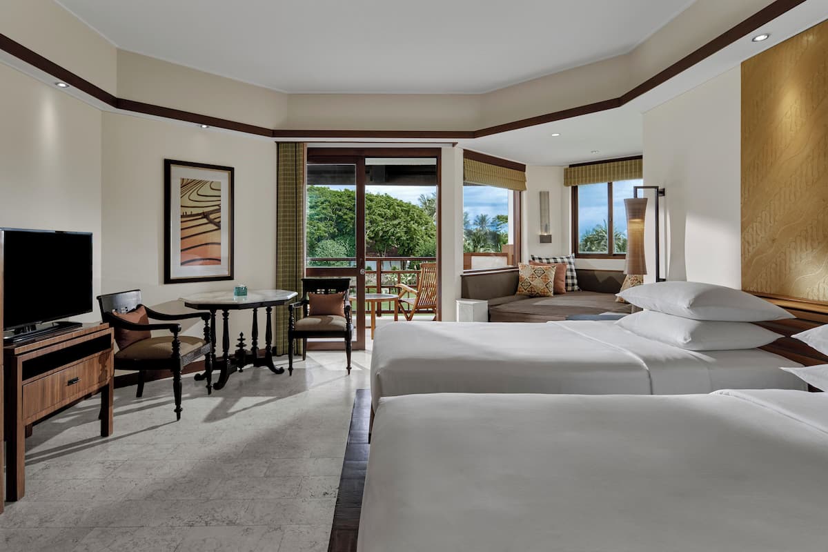 A hotel room with a TV, a small table, two chairs, a sofa, and a large bed.