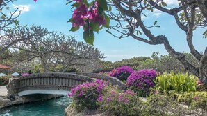 Una fuente tranquila con un puente de piedra, abundante vegetación y flores coloridas.