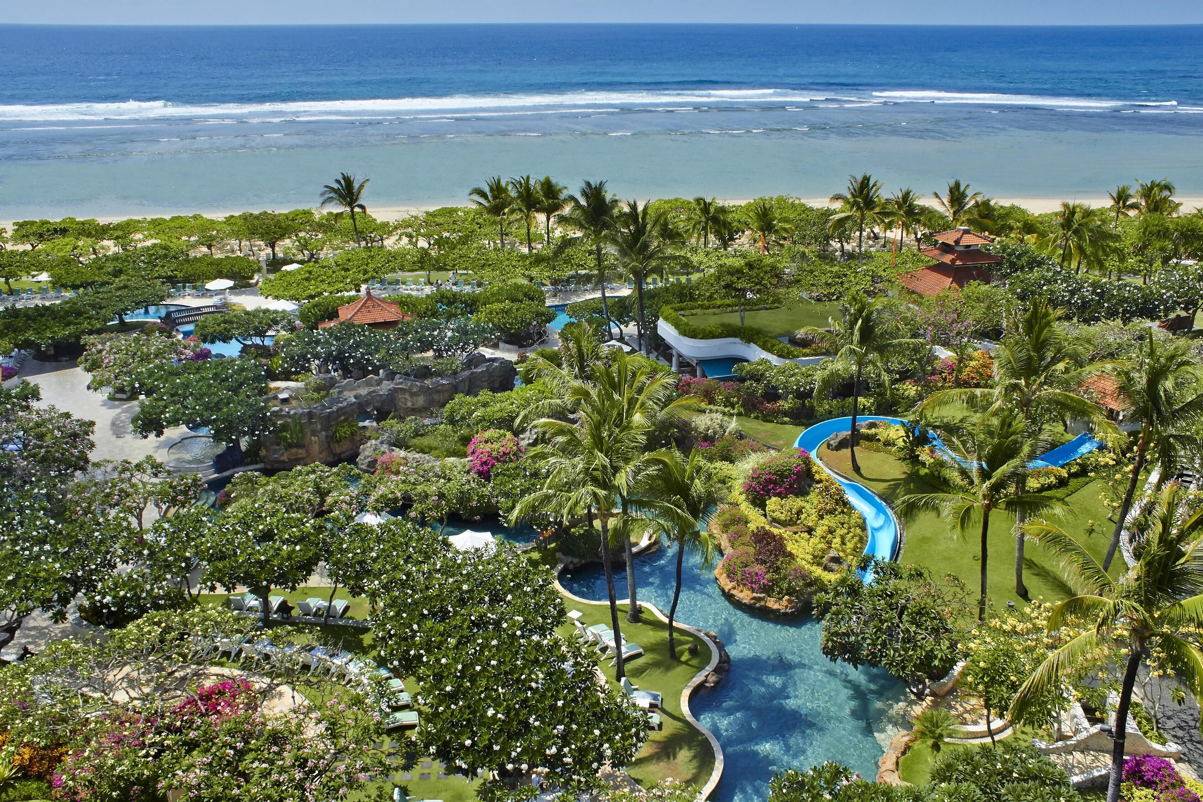 A resort with a pool area, palm trees, and a view of the ocean.