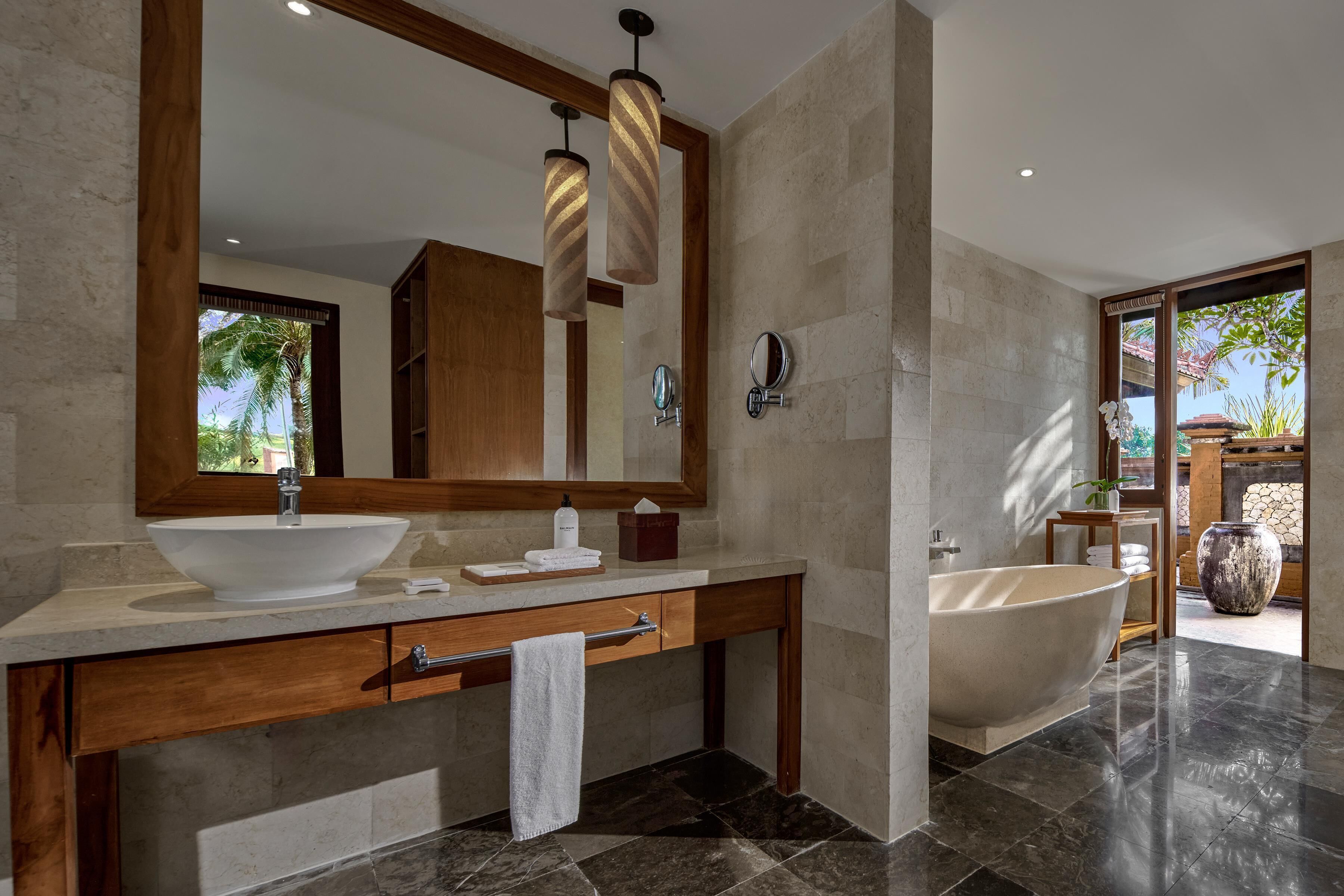 A modern bathroom with a large mirror, a vessel sink, a wooden vanity, a bathtub, and a view of the outdoors.