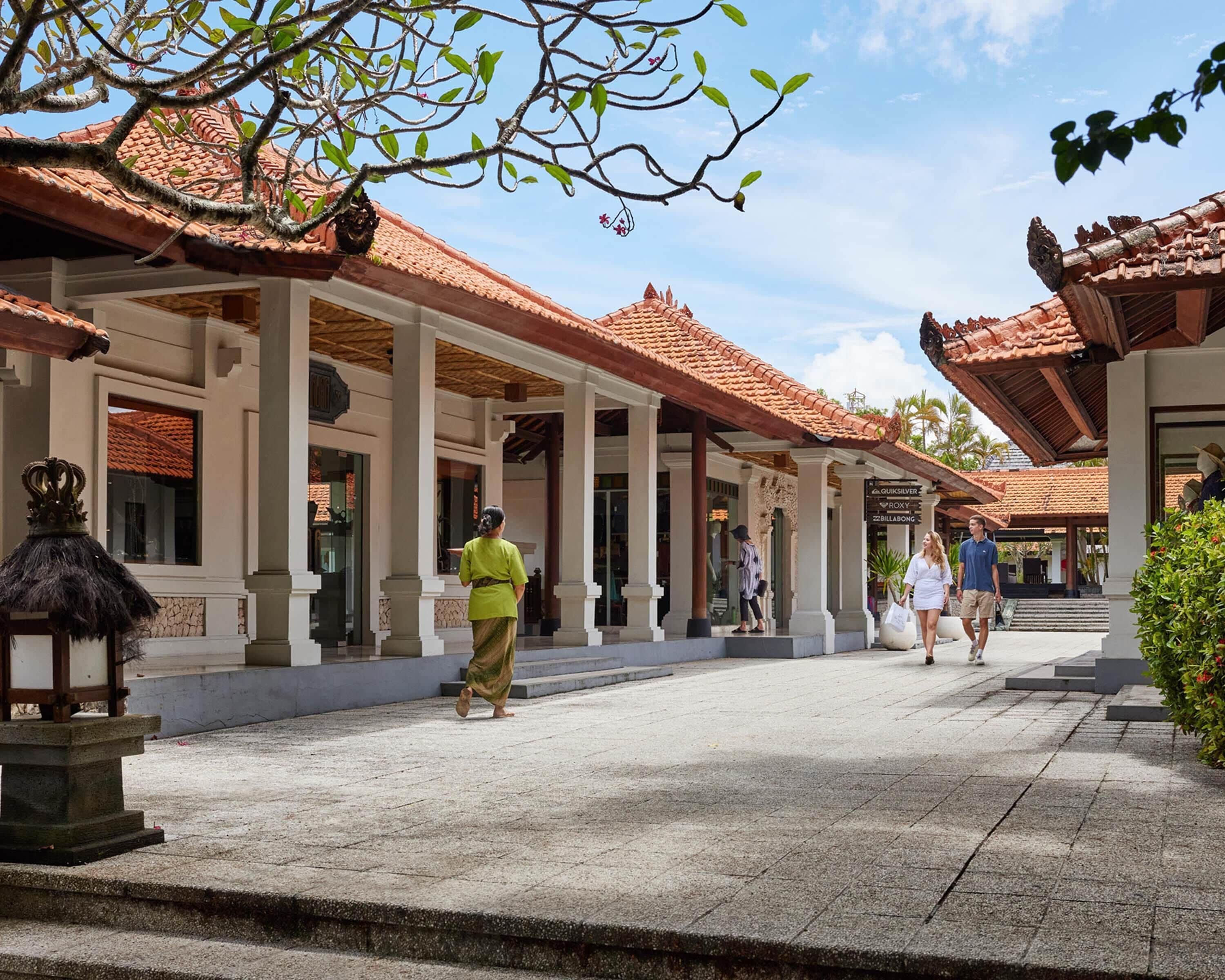 A covered walkway with traditional architecture, including tiled roofs and columns, leading to a building entrance.