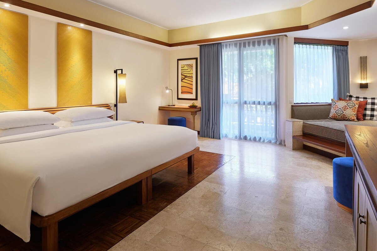 A hotel room with a large bed, a desk, a chair, and a sofa.