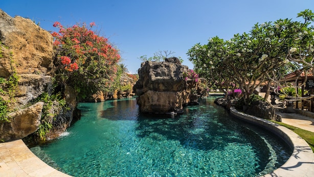Una piscina cristalina con una roca central, rodeada de abundante vegetación y un sendero de piedra.