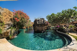 A clear pool with a rock centerpiece, surrounded by lush greenery and a stone pathway.