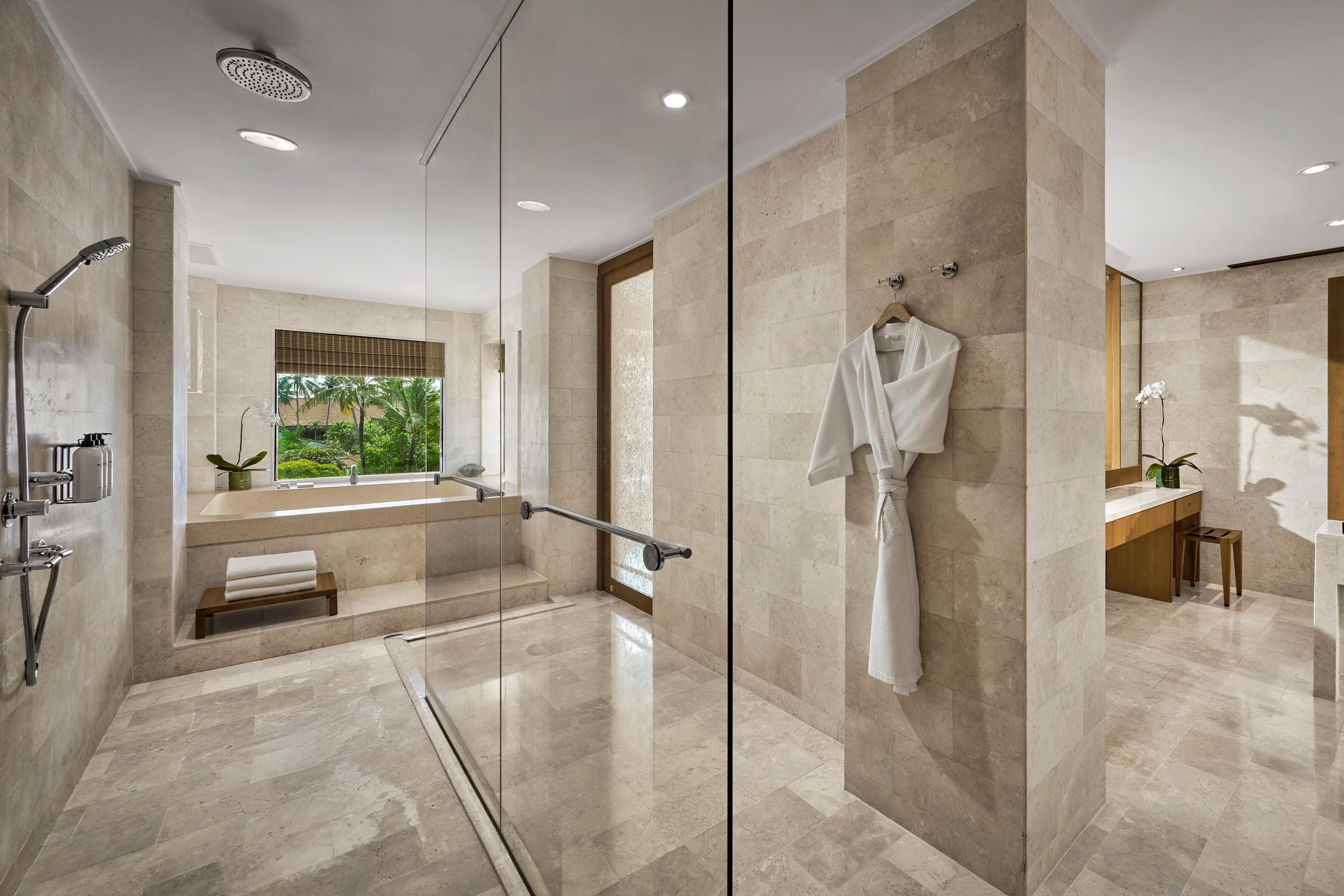 Un baño moderno con ducha de vidrio, bañera y ventana grande con vistas a la vegetación.