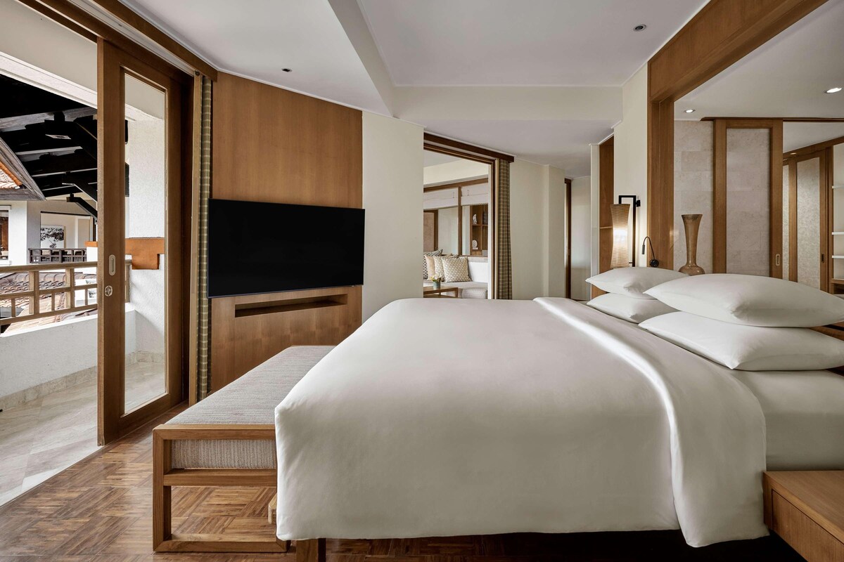 A modern bedroom with a large bed, wooden headboard, and a TV mounted on the wall.
