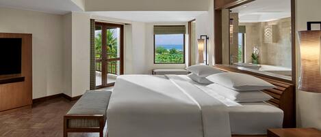 A hotel room with a large bed, a TV, a wooden bench, and a balcony with a view of the ocean.