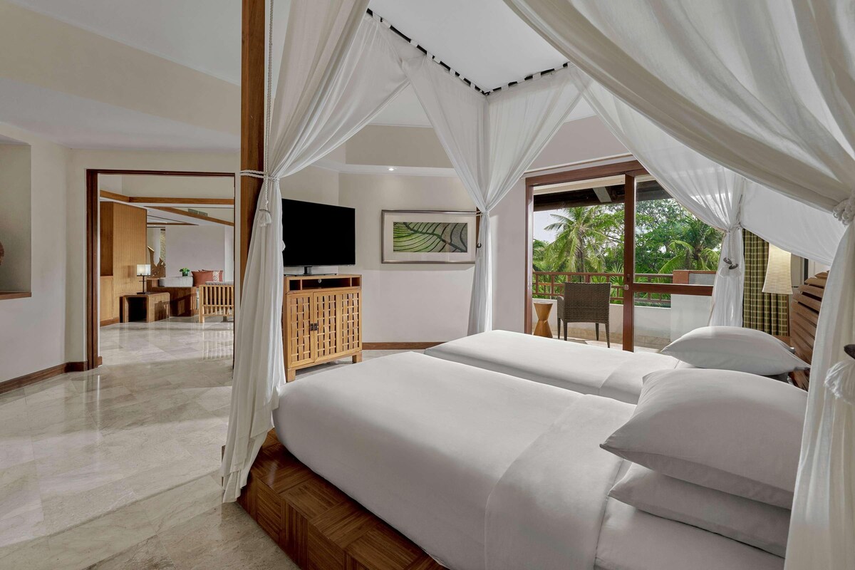 A hotel room with a large bed, a TV, and a balcony with a view of palm trees.