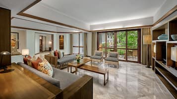 A spacious living area with a sofa, armchairs, a coffee table, and a TV. There is a large window providing a view of greenery outside.