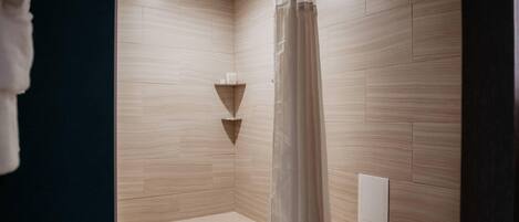 A modern shower area with a wooden floor, a shower curtain, and a small shelf with toiletries.
