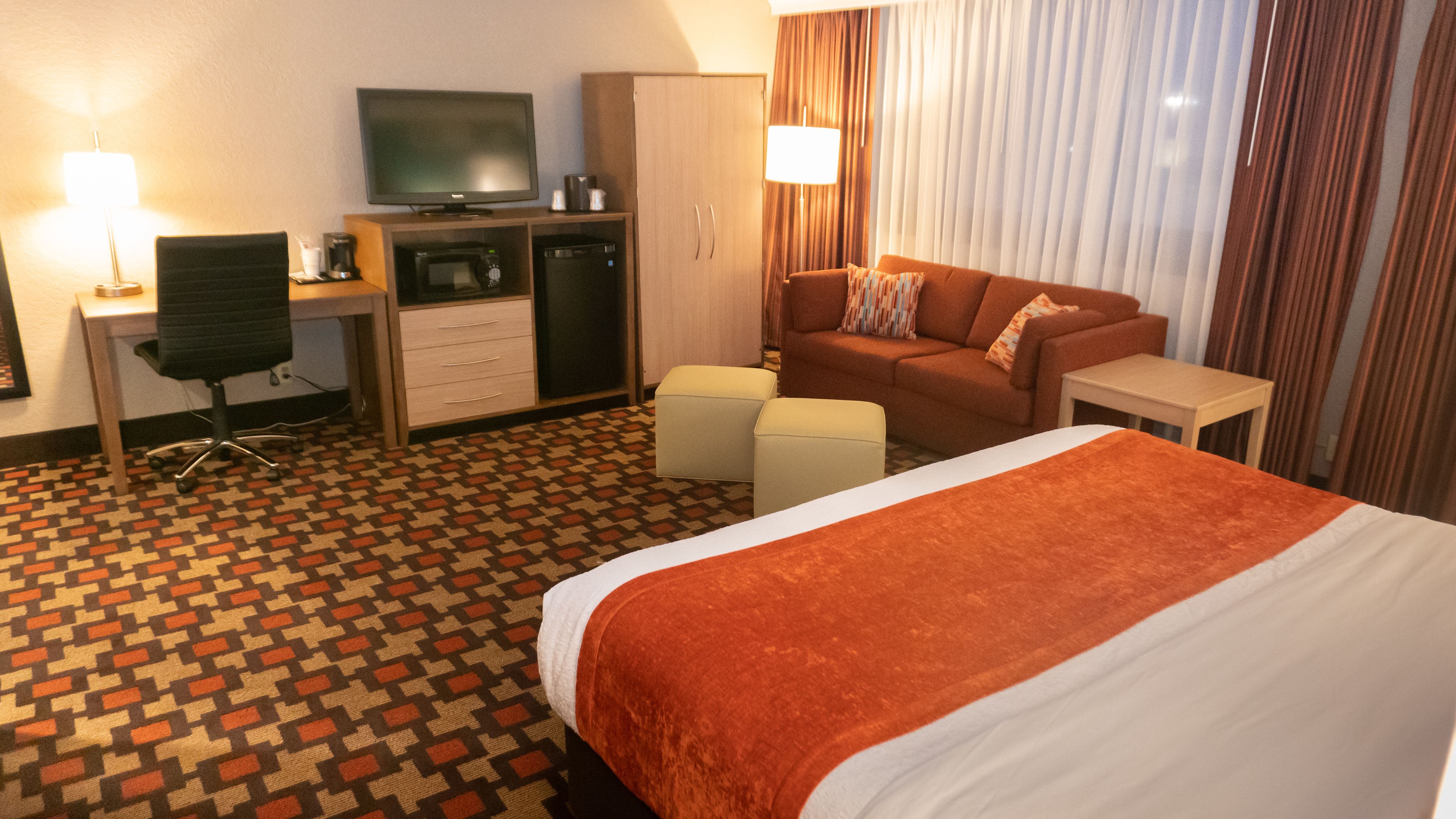 A hotel room with a bed, a desk with a computer, a television, a sofa, and a small table.
