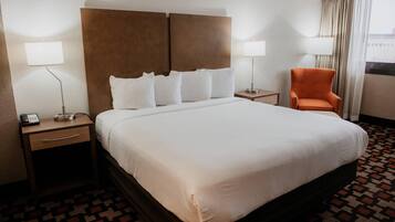 A hotel room with a large bed, two bedside tables, a chair, and a window with curtains.