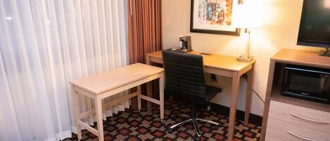 Habitación de hotel con un escritorio de madera, una silla de oficina negra, un televisor y un cuadro en la pared.