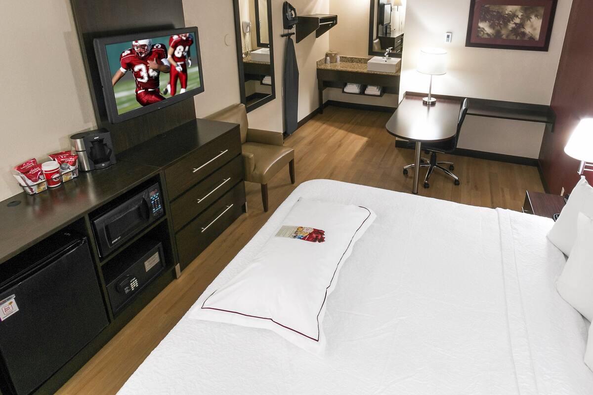 A hotel room with a bed, a desk, a television, a mirror, and a small kitchenette.