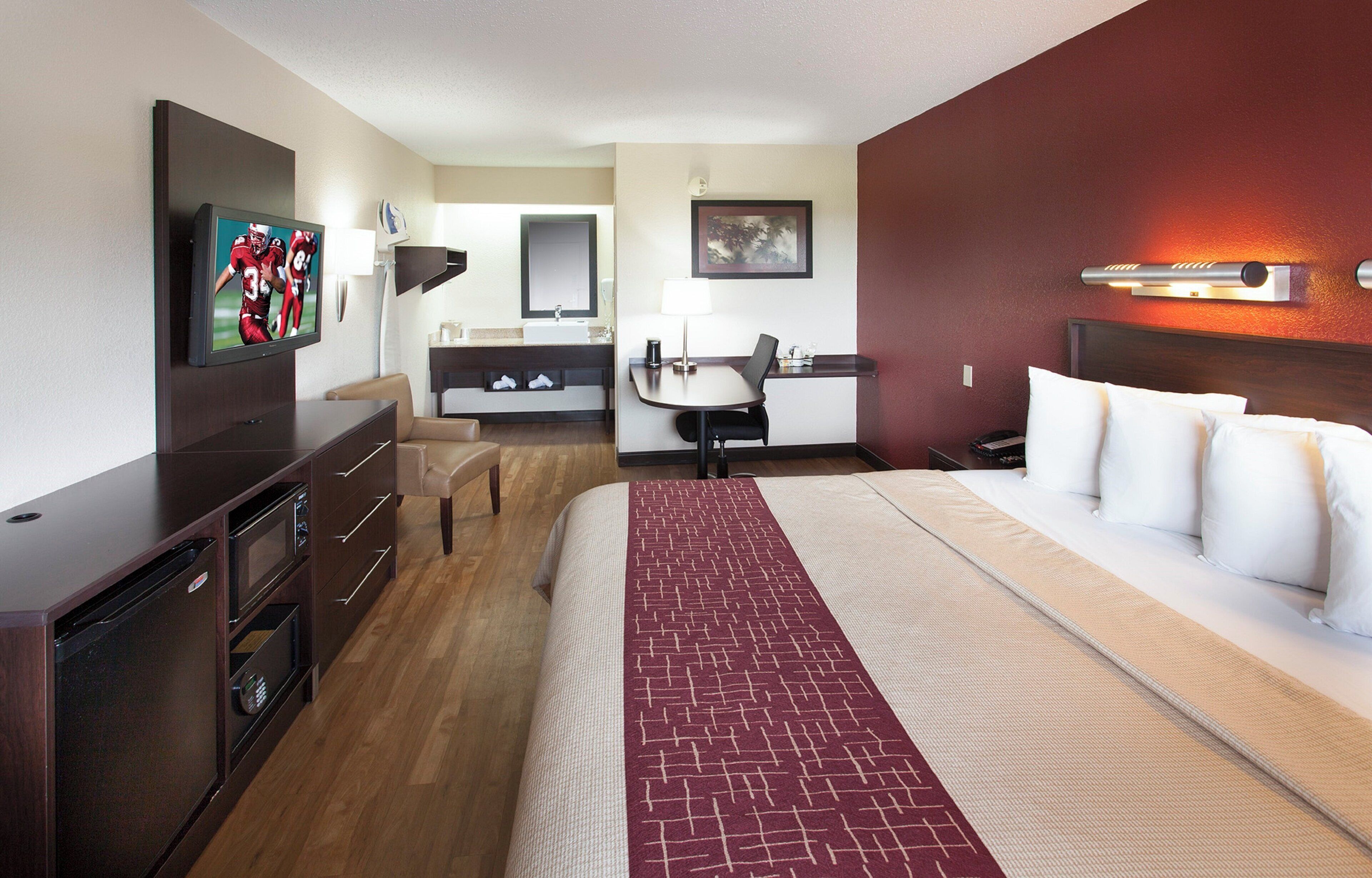 Habitación de hotel con cama, escritorio, silla, televisor y baño.
