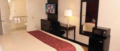 A hotel room with a bed, a desk, a chair, a television, a mirror, a lamp, and a microwave.