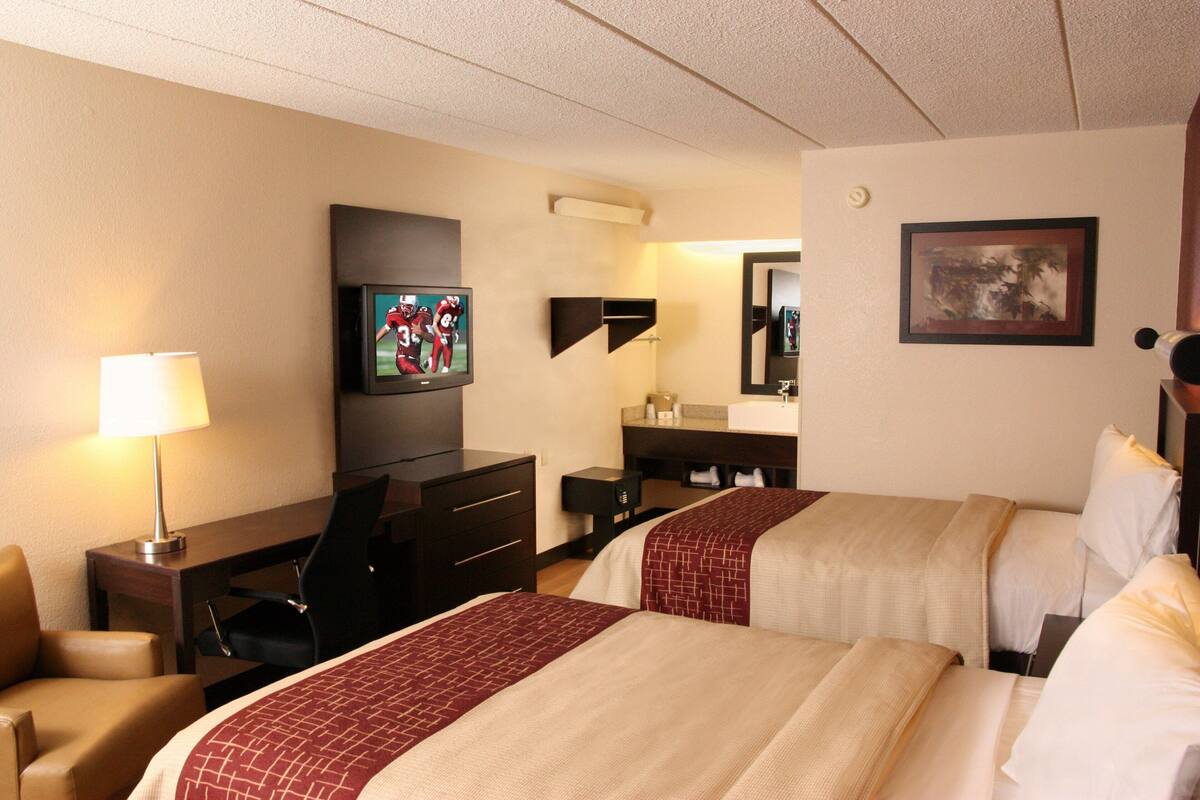 A hotel room with two beds, a desk, a chair, a TV, and a bathroom.