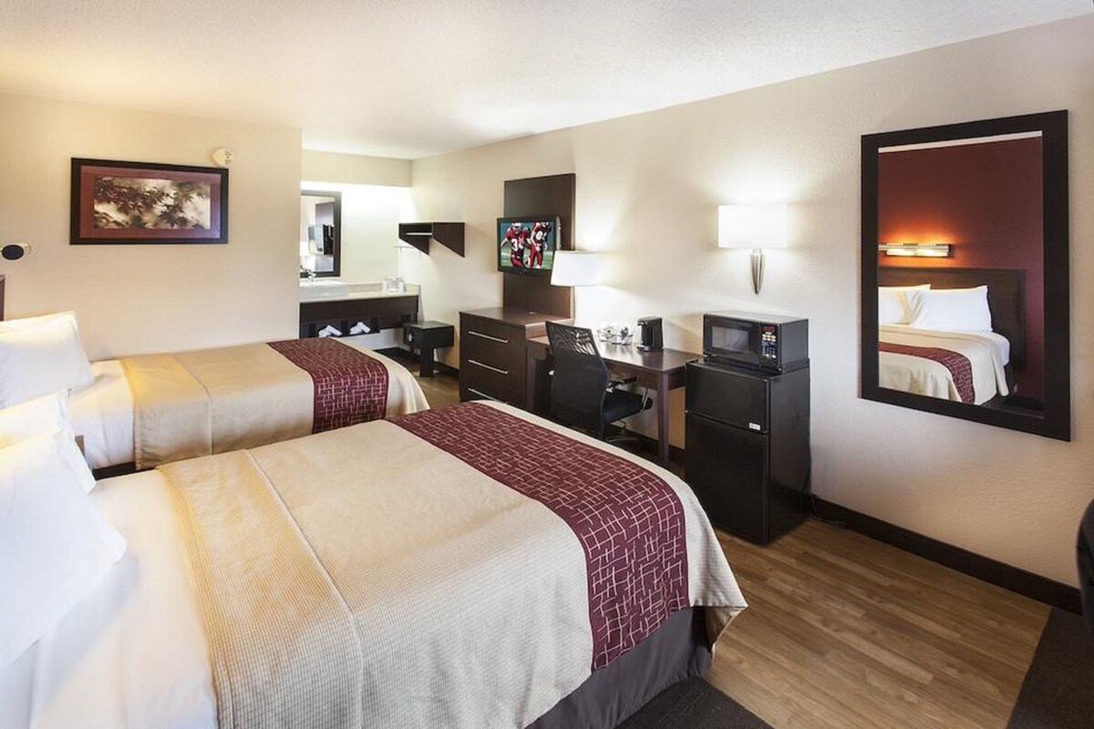 A hotel room with two beds, a desk, a chair, a TV, and a mirror.