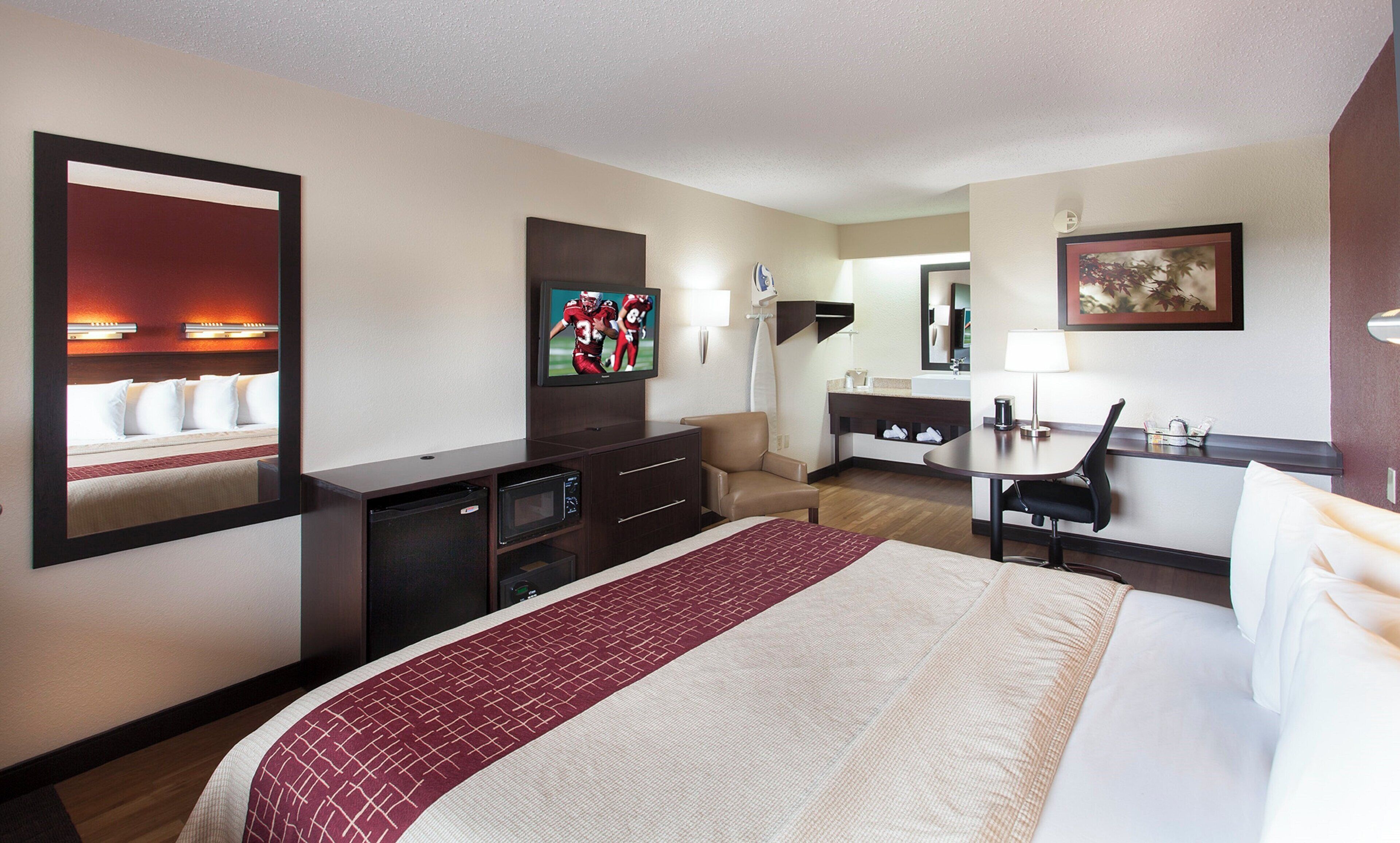 A hotel room with a bed, a desk, a chair, a television, and a mirror.