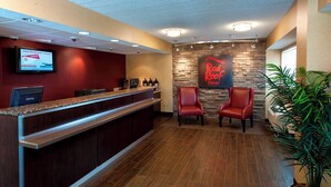 A reception area with a counter, two red chairs, a Red Roof Inn sign, and a monitor displaying a RedCard advertisement. - Red Roof Inn PLUS+ Philadelphia Airport (Essington)