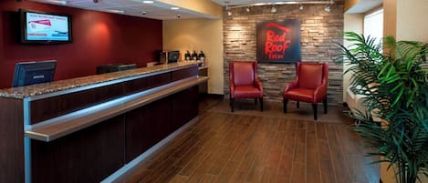 A reception area with a counter, two red chairs, a Red Roof Inn sign, and a monitor displaying a RedCard advertisement.