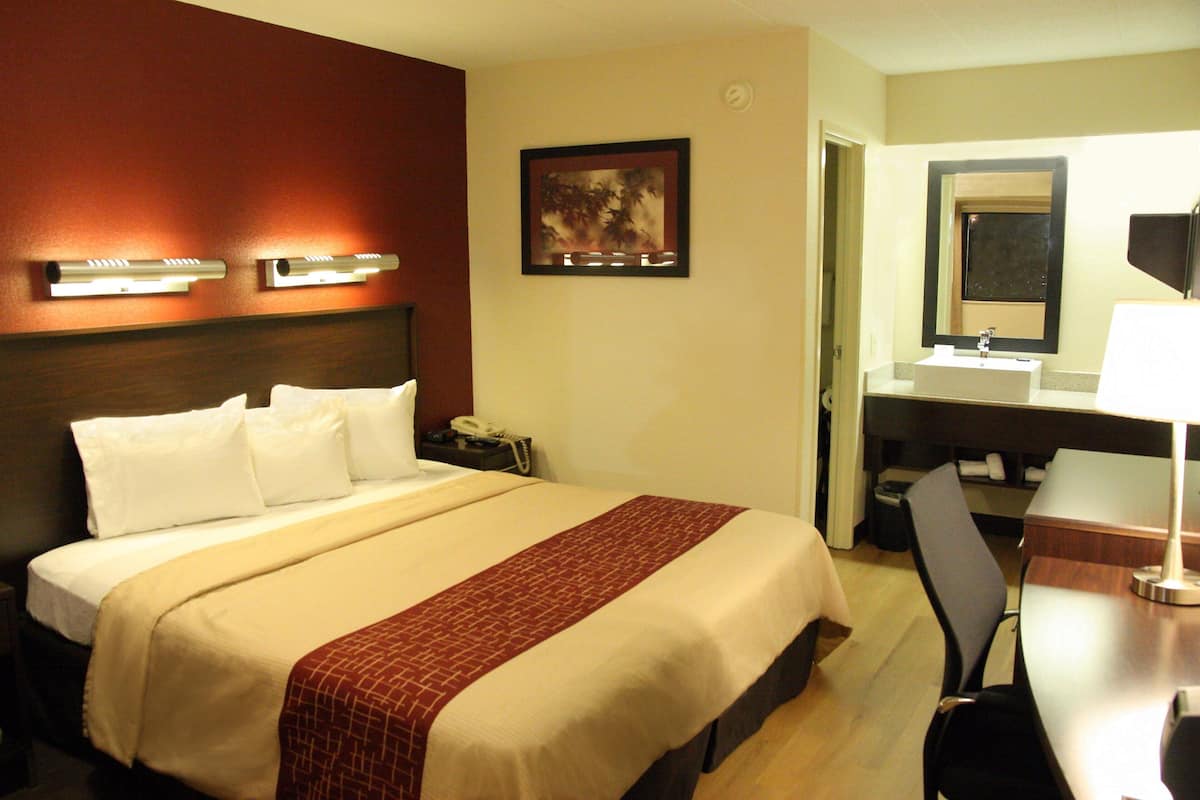 A hotel room with a bed, bedside table, lamp, and a desk with a chair.