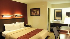 A hotel room with a bed, bedside table, lamp, and a painting on the wall. - Red Roof Inn PLUS+ Philadelphia Airport (Essington)