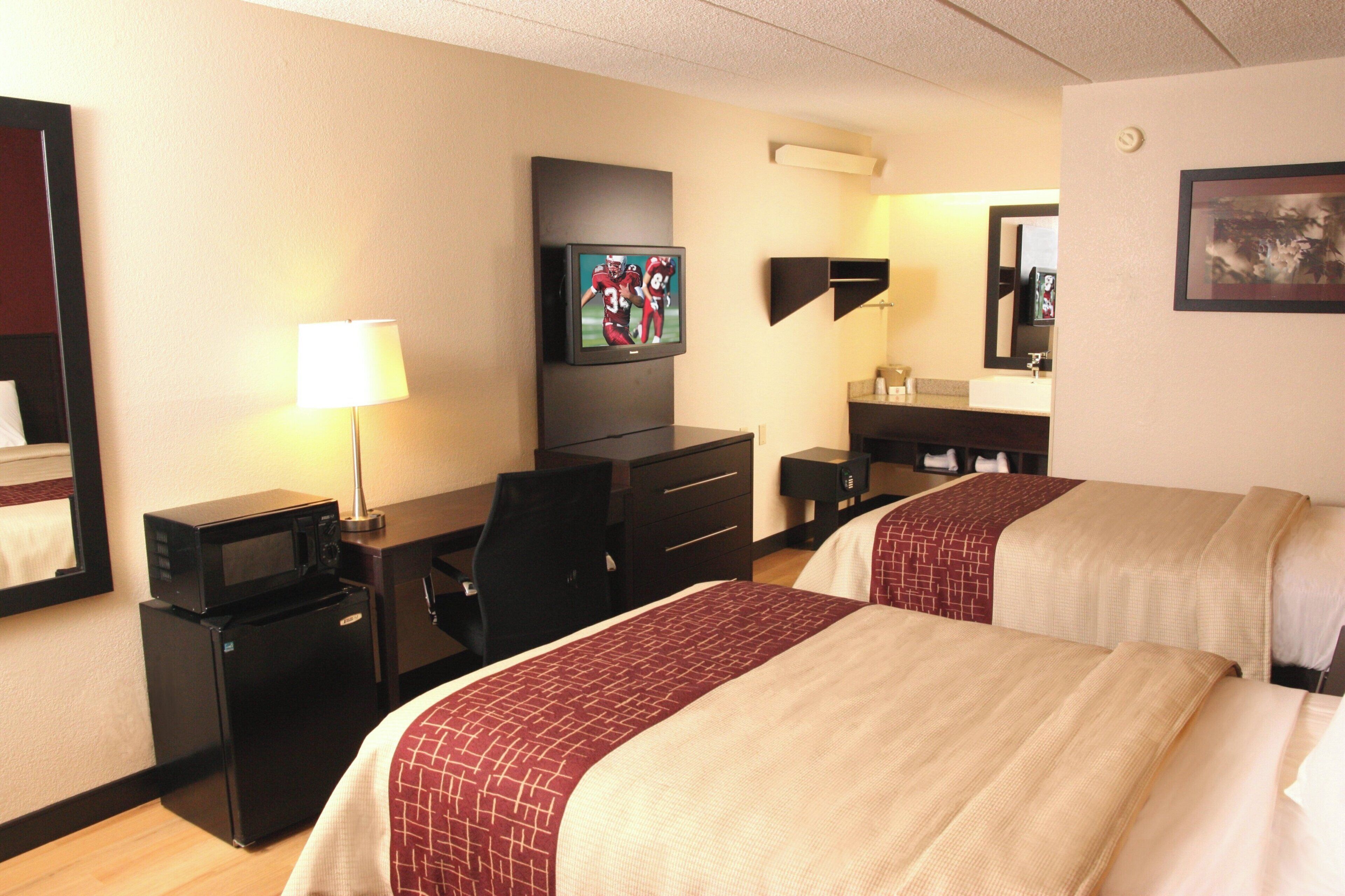 A hotel room with two beds, a desk, a television, a lamp, and a mirror.