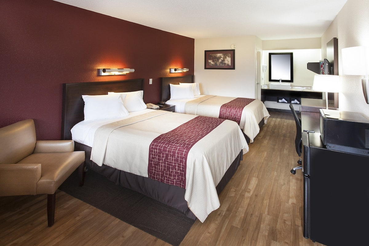 A hotel room with two beds, a desk, a chair, a desk lamp, and a mirror.