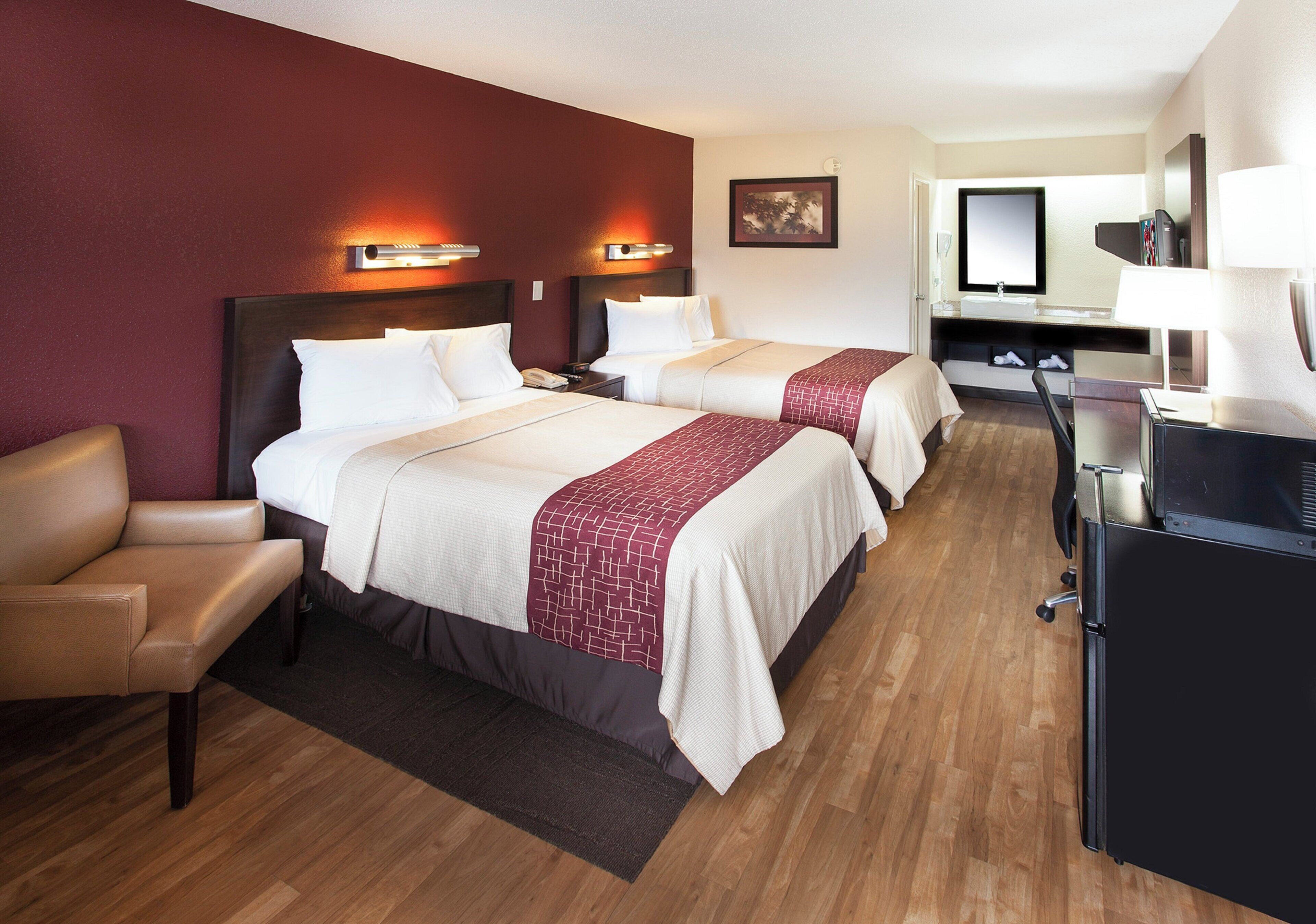 A hotel room with two beds, a desk, a chair, and a bathroom.