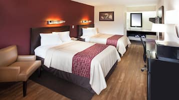 A hotel room with two beds, a desk, a chair, and a bathroom.