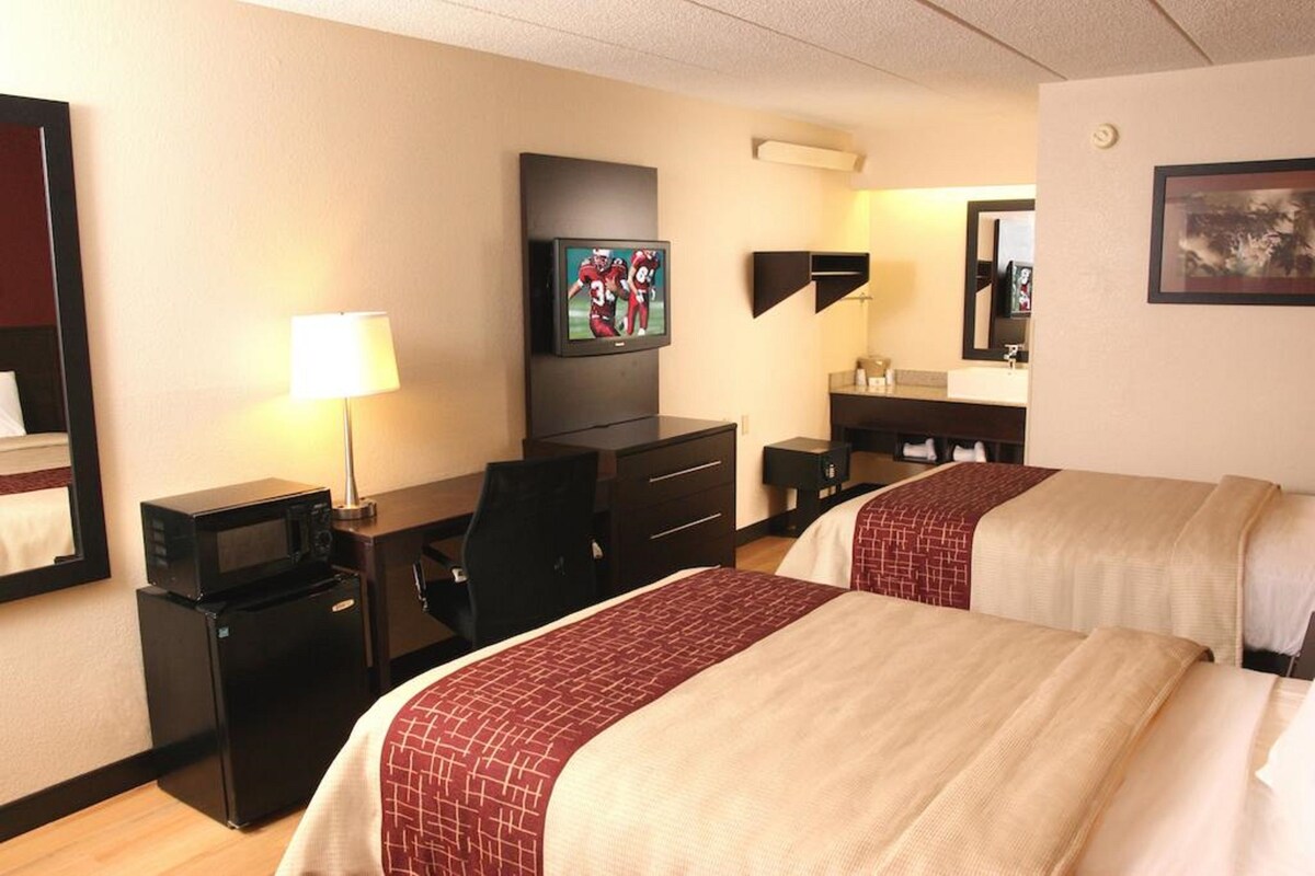 A hotel room with two beds, a desk with a computer, a television, a microwave, and a refrigerator.