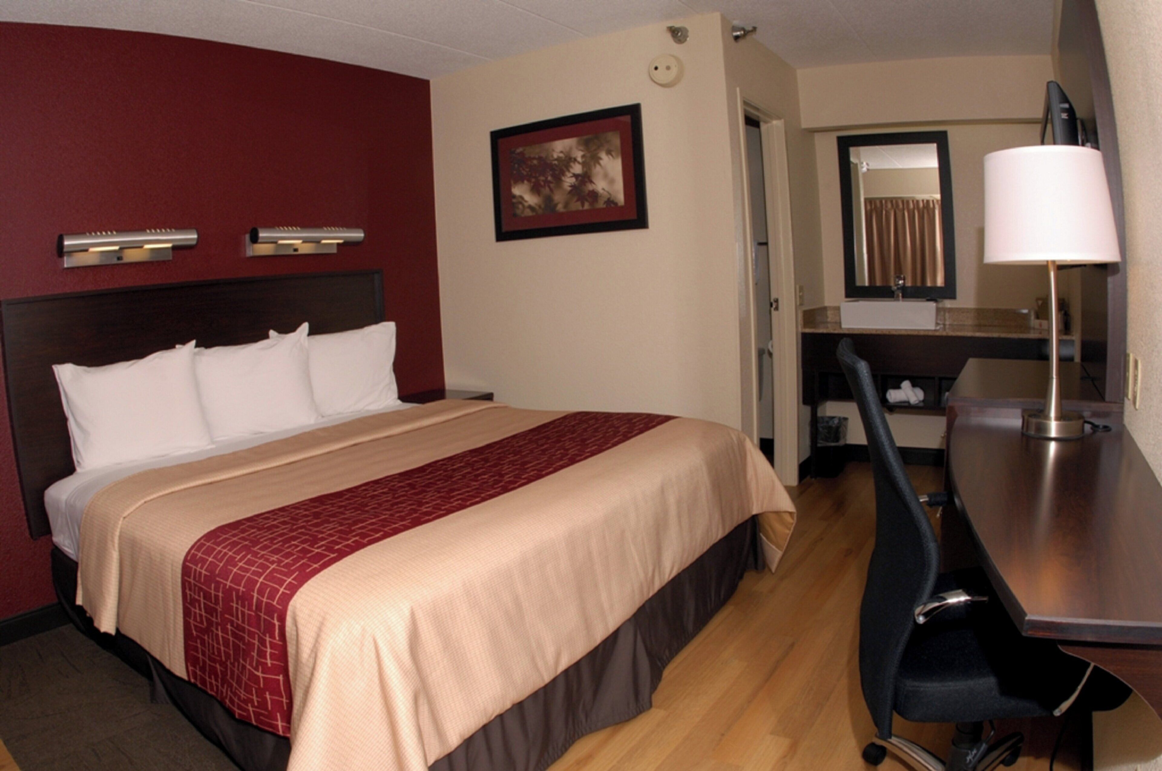Une chambre d’hôtel avec un lit, un bureau, une chaise, un miroir et un tableau au mur.