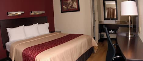A hotel room with a bed, a desk, a chair, a mirror, and a picture on the wall.