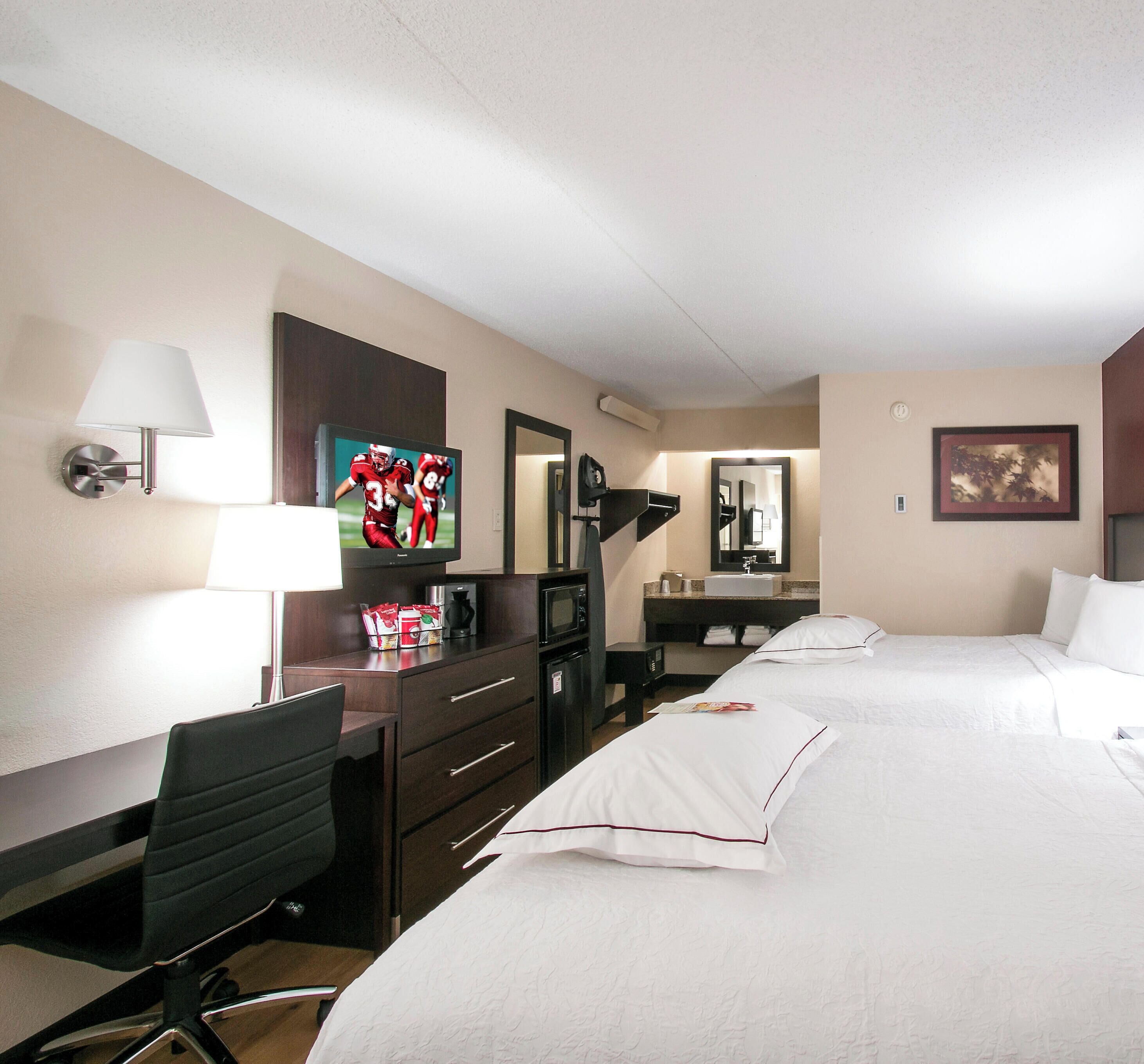 A hotel room with a bed, desk, chair, TV, and a bathroom mirror.
