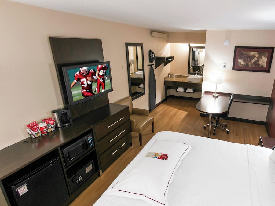 A hotel room with a TV, a desk, a chair, a bed, a desk lamp, and a bathroom visible in the background.
