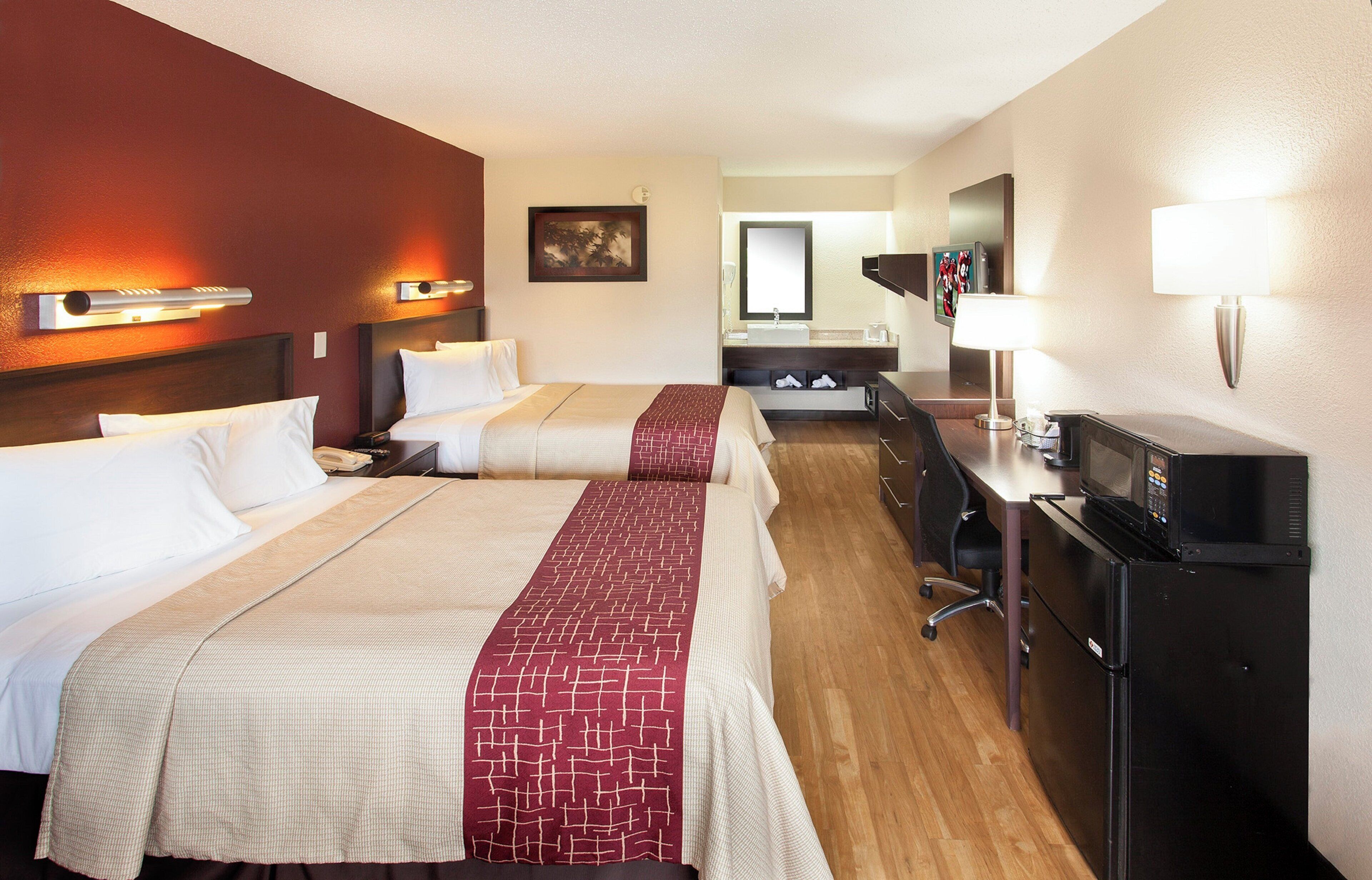A hotel room with two beds, a desk, a television, and a microwave.