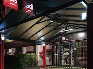 A hotel entrance with a covered walkway, a glass door with 'WELCOME' signage, and a red 'HOTELS' sign above.