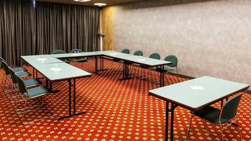 Une salle de conférence équipée de tables, de chaises, d’un tapis à motifs et d’un rideau en fond.