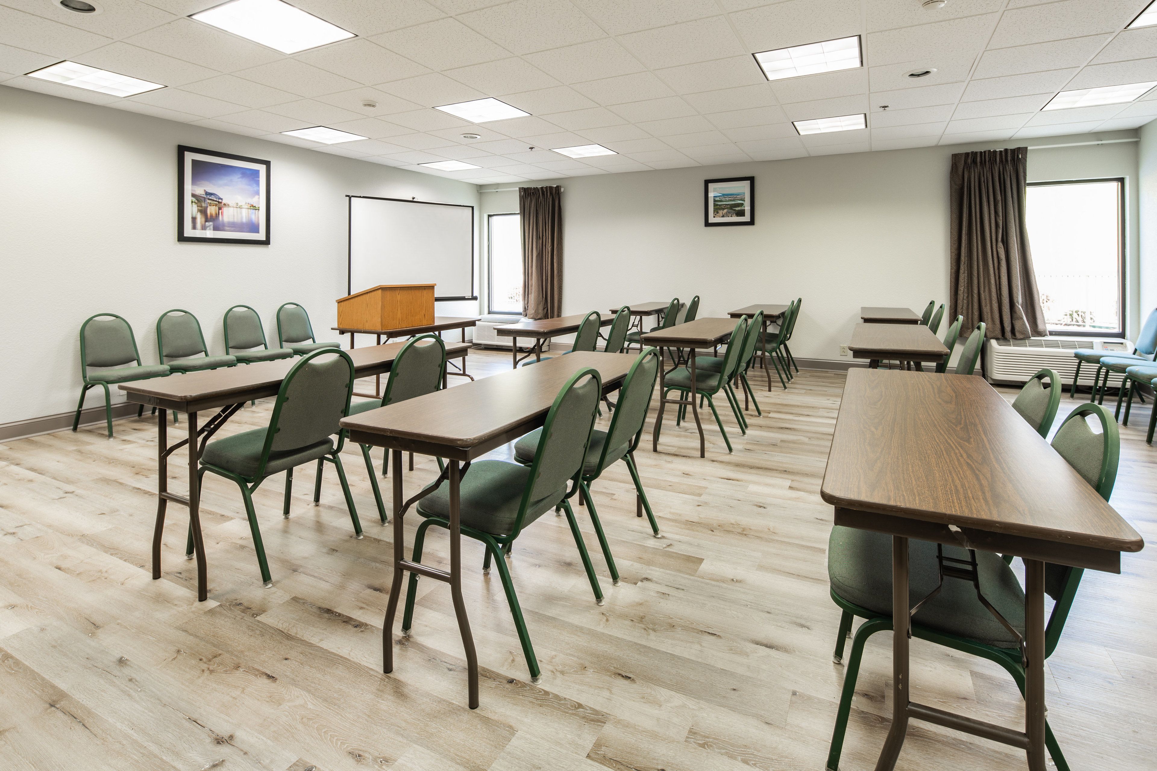 A conference room with multiple tables and chairs, a podium, and two large windows with curtains.