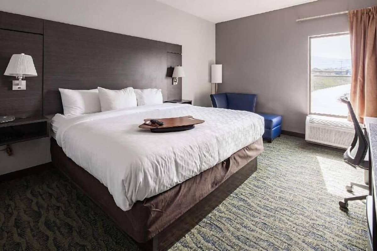 Hotellihuone, jossa on suuri sänky, työpöytä lampun kanssa, tuoli ja näkymä ulos.
