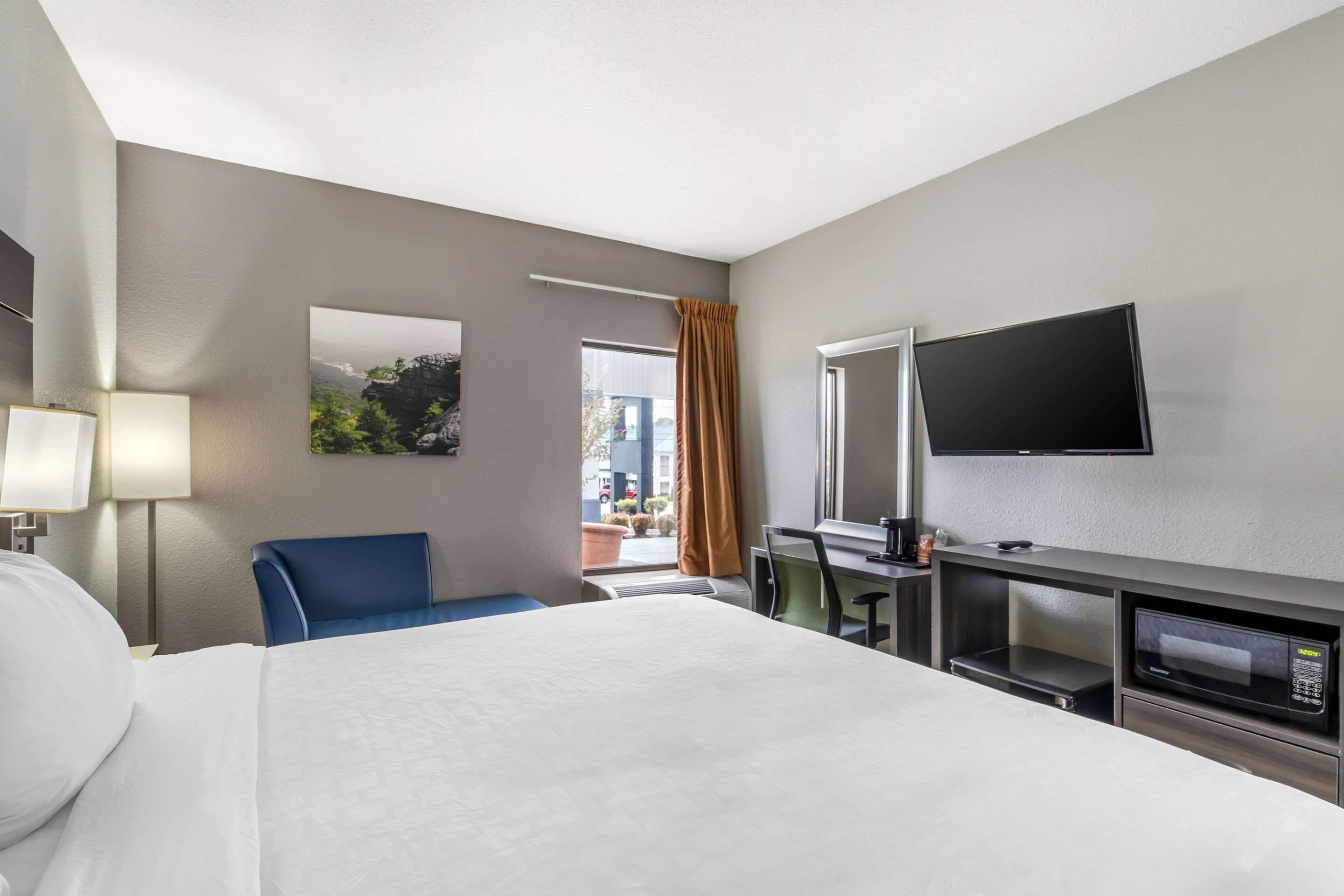 Habitación de hotel con cama, escritorio con computadora, televisor y ventana con cortinas.
