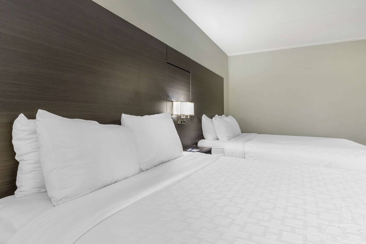 Hotellihuone, jossa on kaksi sänkyä, yöpöytä, lamppu ja tumma puinen pääty.