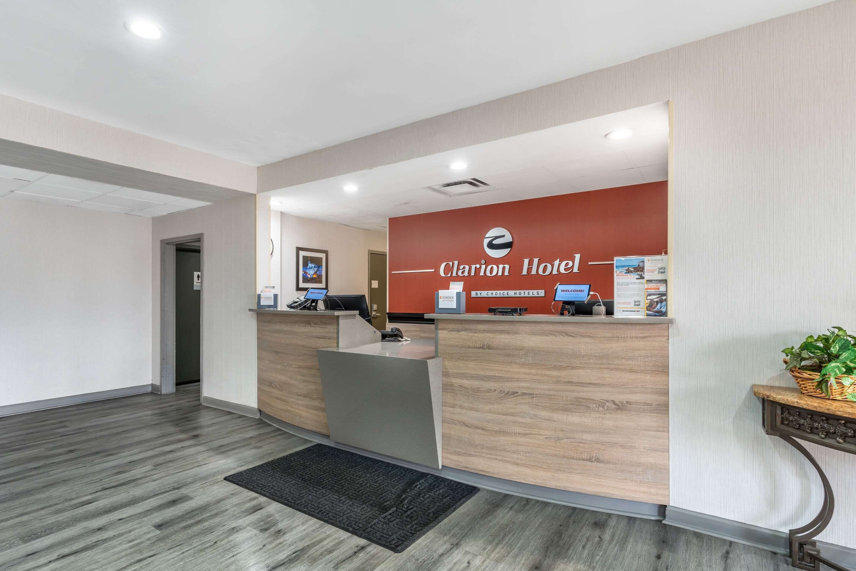 A hotel reception area with a wooden reception desk, a sign for Clarion Hotel, and a framed picture on the wall.
