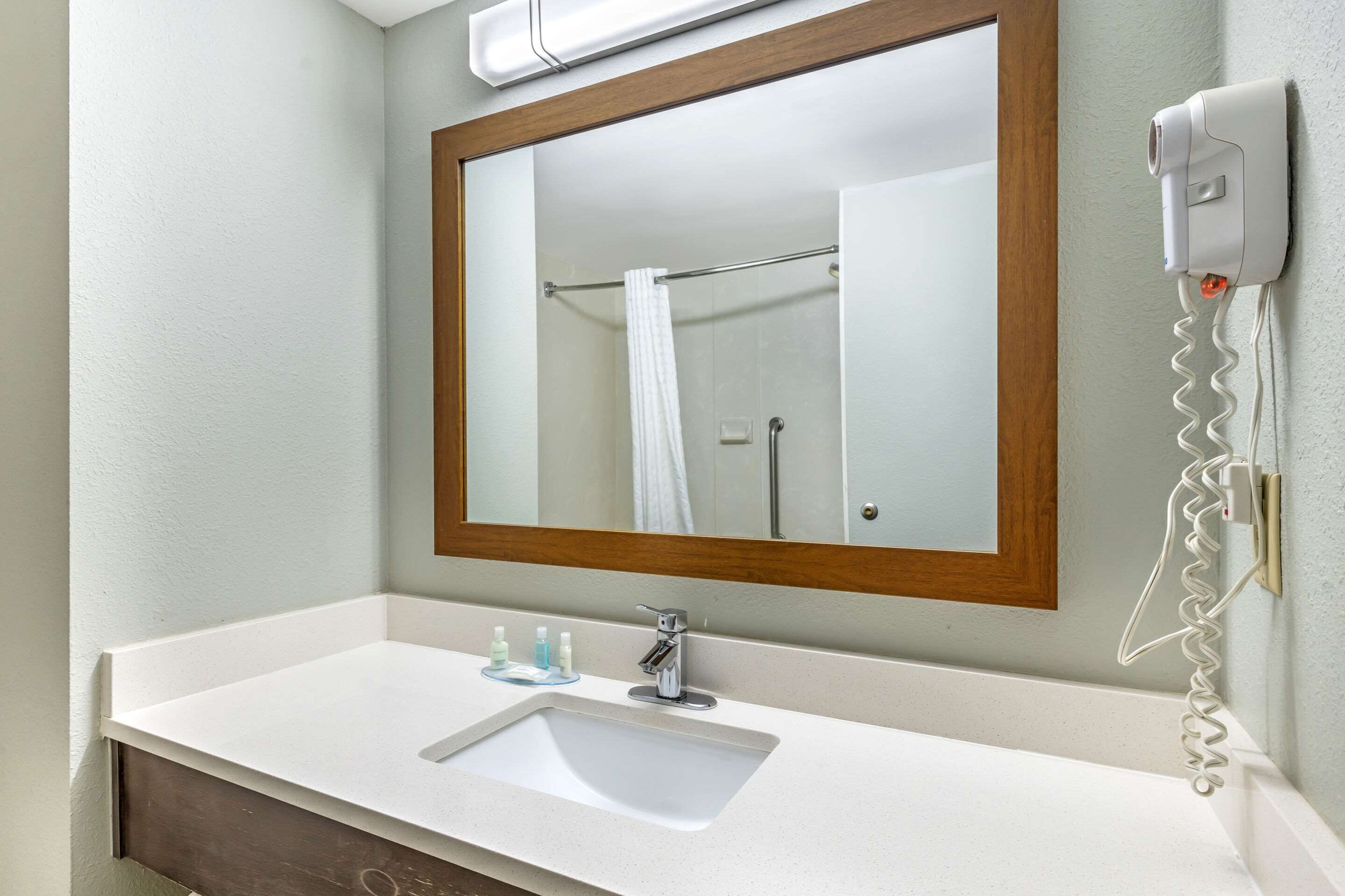 A bathroom with a white sink, a mirror with a wooden frame, and a hairdryer mounted on the wall.